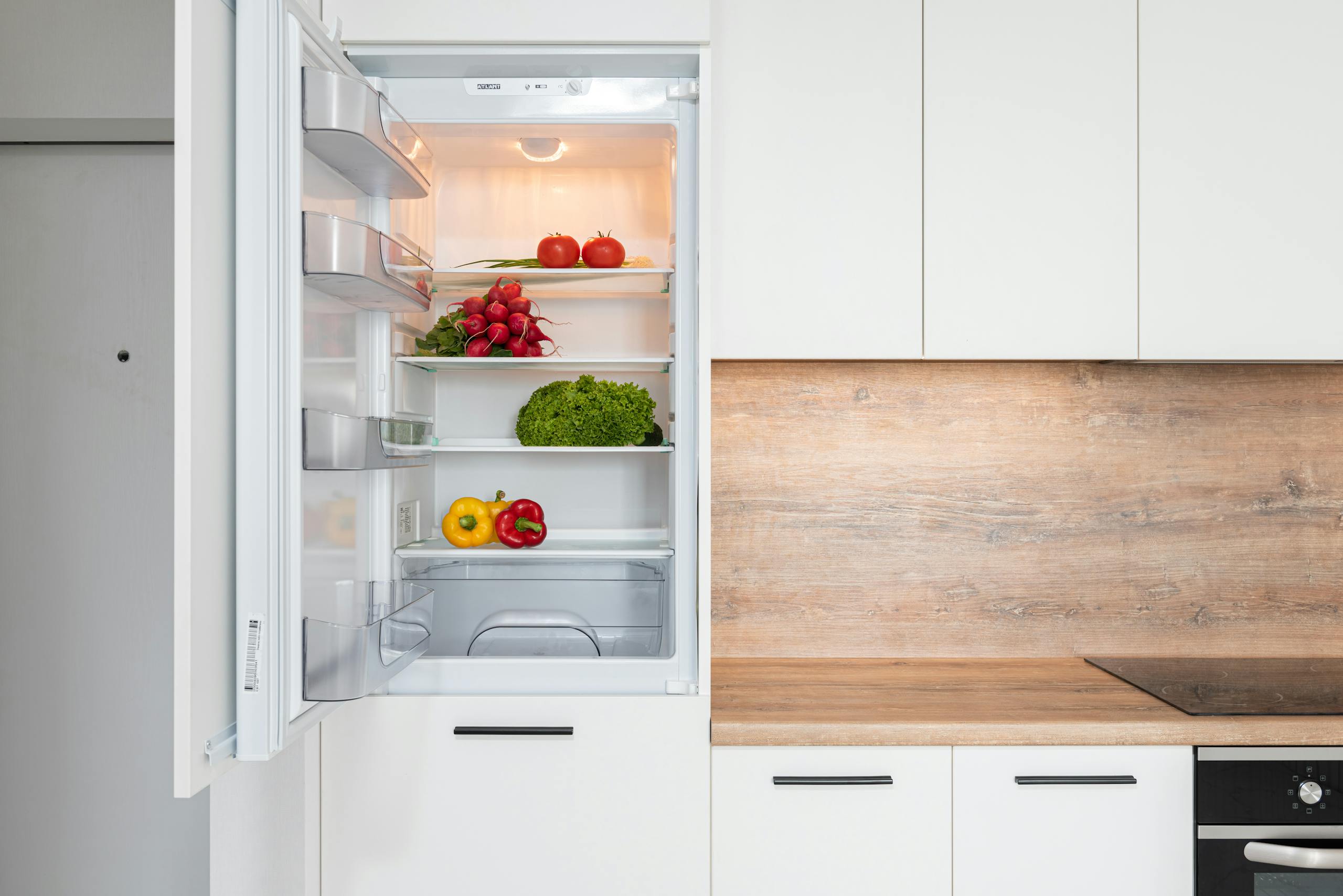 Open fridge in a sleek kitchen with fresh vegetables, perfect for healthy meals.