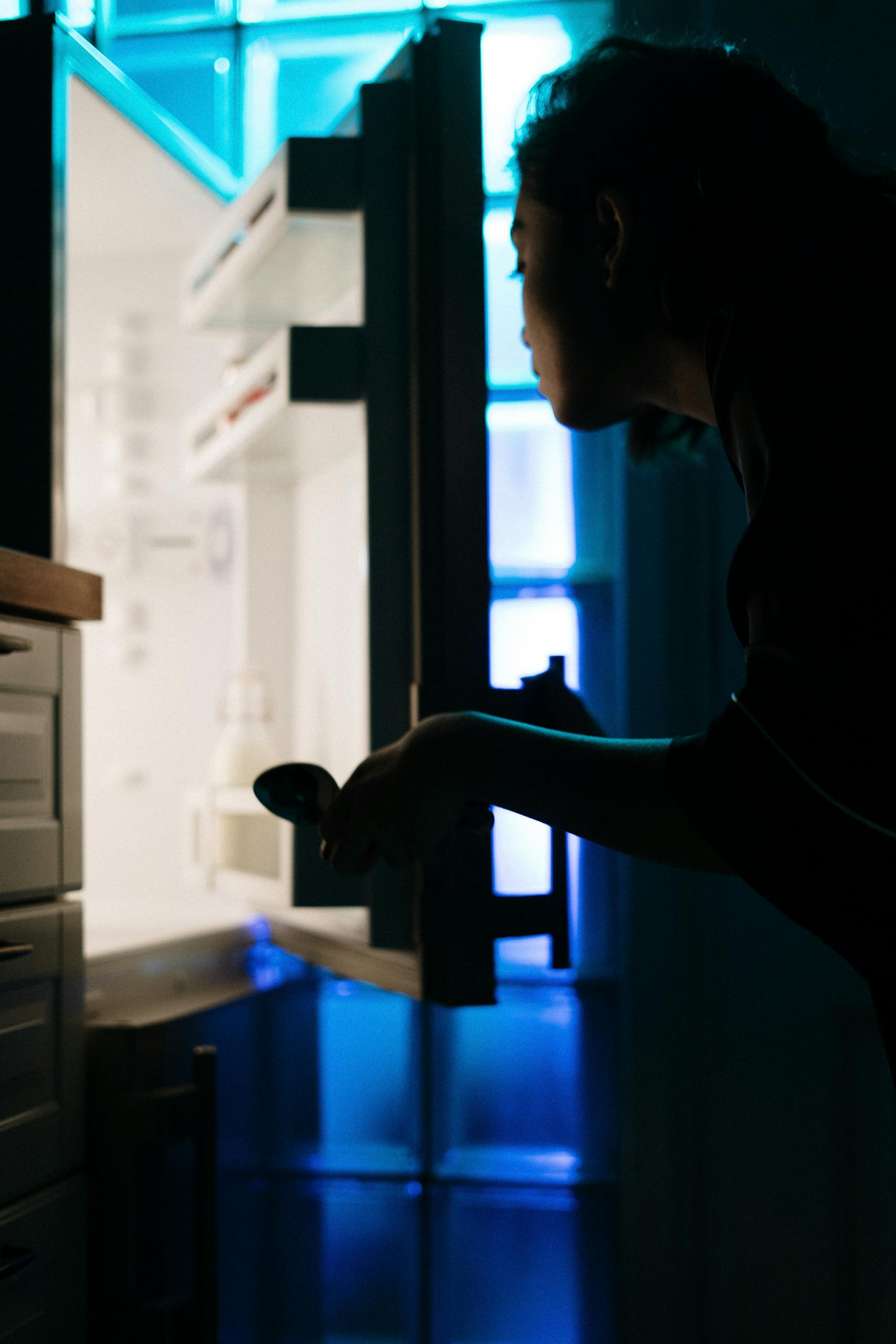 Silhouette of a woman checking an empty fridge at night with neon light.