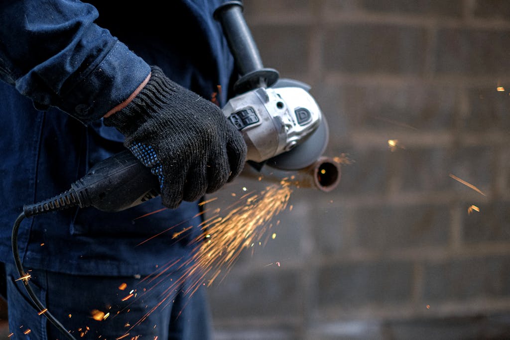 Worker using angle grinder for metalwork, generating bright sparks indoors.