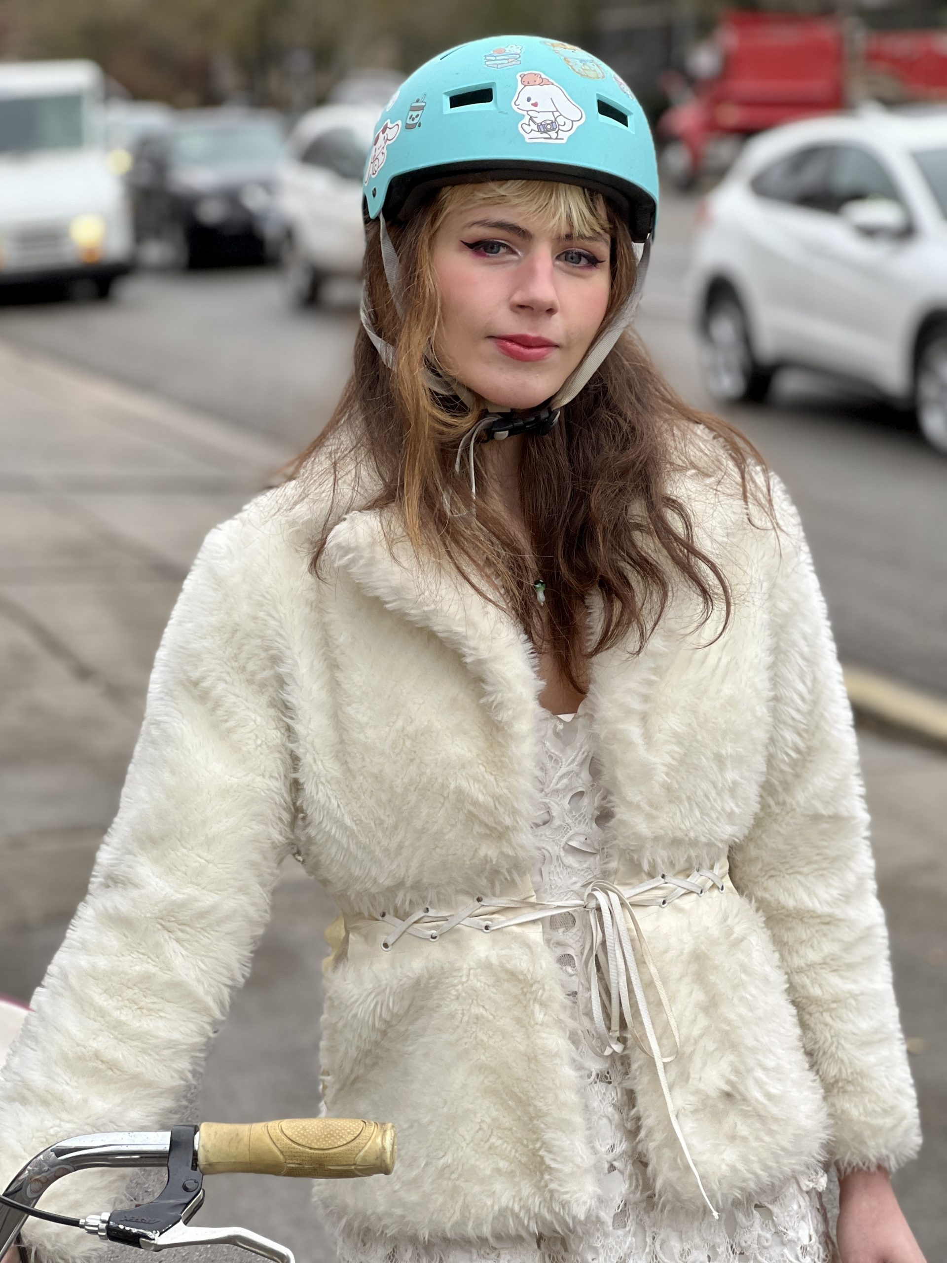 Cellist Ari Scott with white fake fur winter coat and turquoise bike helmet