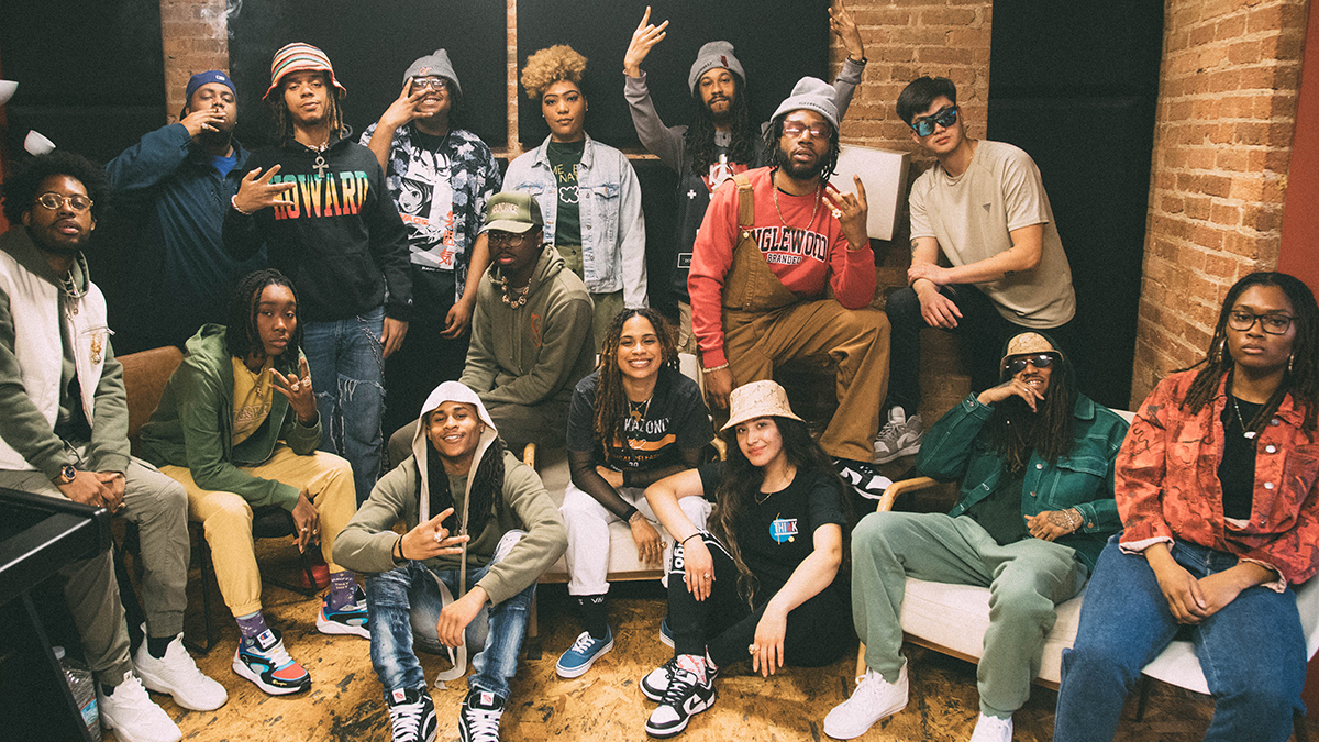 a group of 15 people sit and stand in a posed arrangement in what looks like a lounge or even a live room in a recording studio