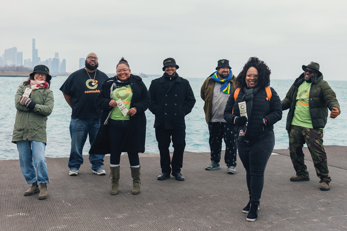 seven adults dressed for winter stand on the concrete edge of Lake Michigan