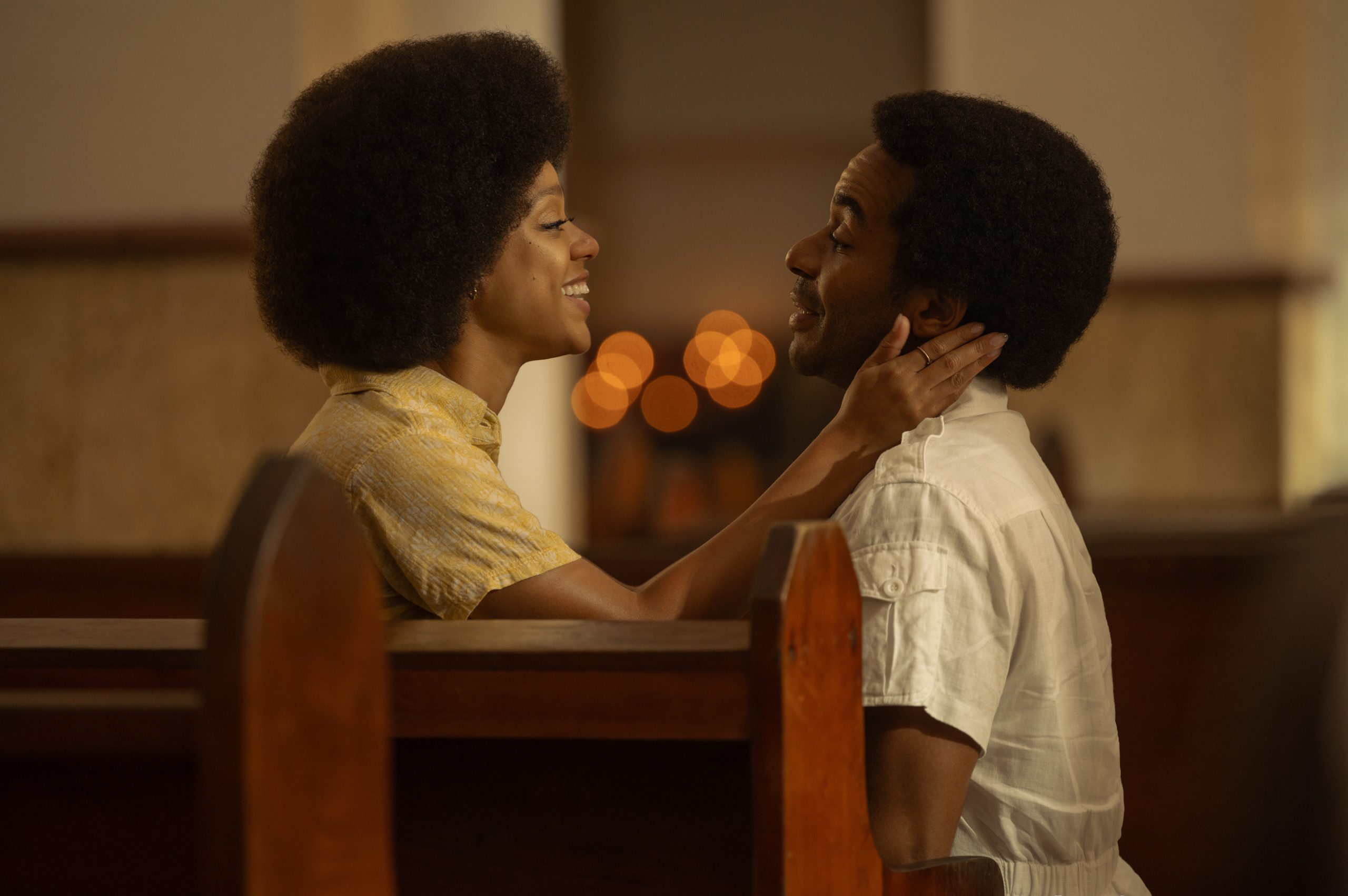 a young Black woman holds the face of a young Black man in church pews