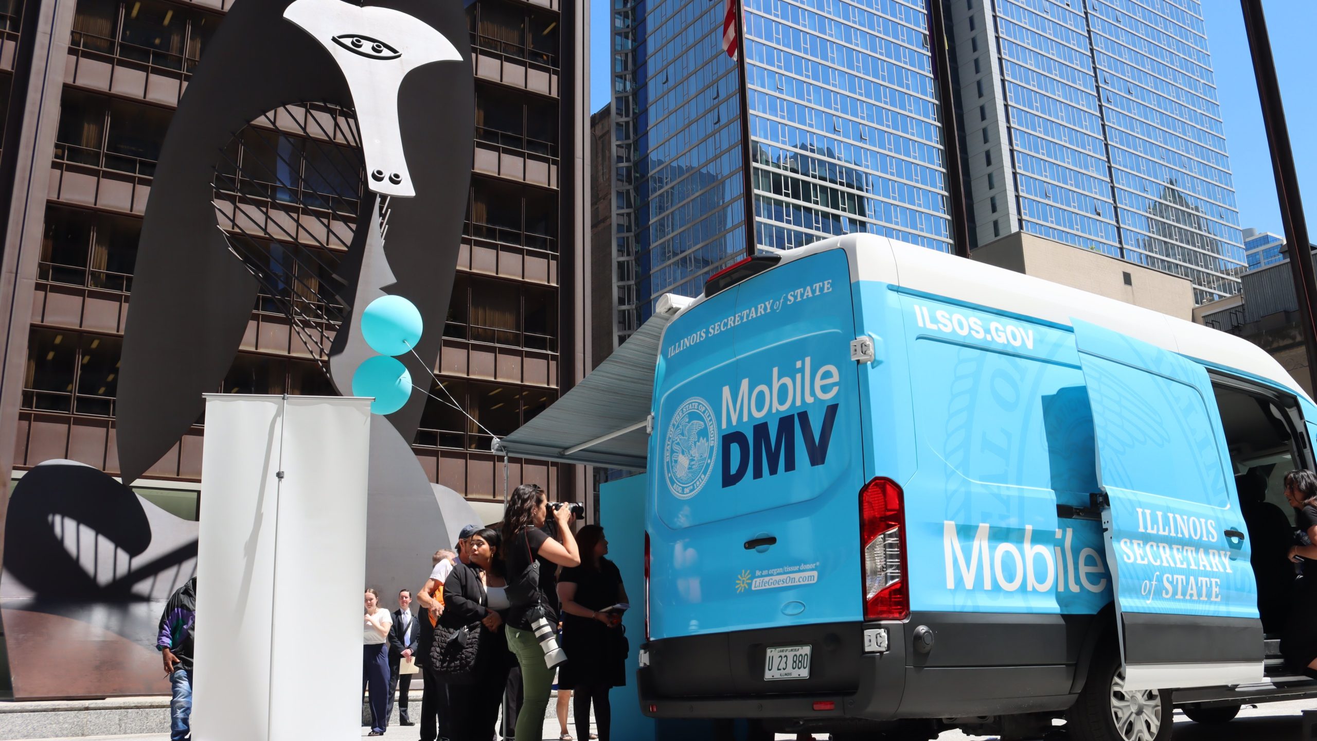 A bus parked in front of a buidling and a Picasso statute in downtown Chicago