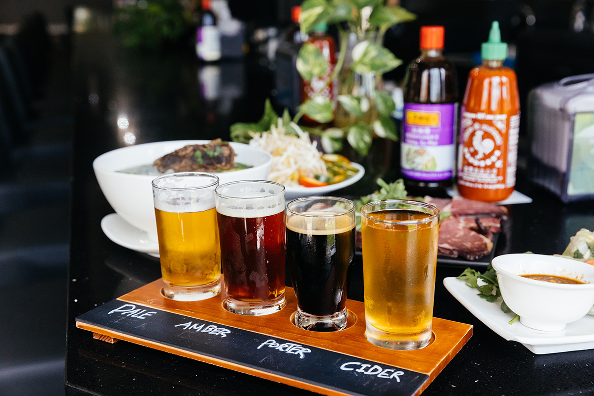 a flight of four small beers on a table with Vietnamese food and condiments