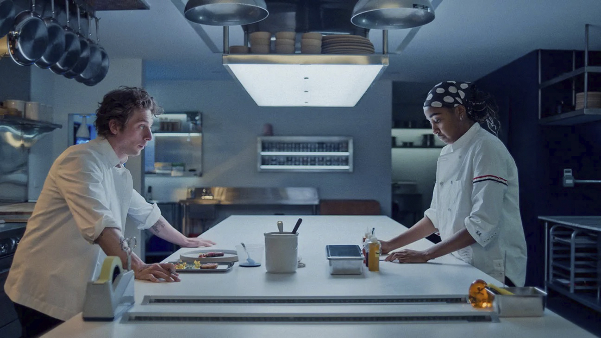 two chefs, a white man and Black woman, stand in a minimalist restaurant kitchen