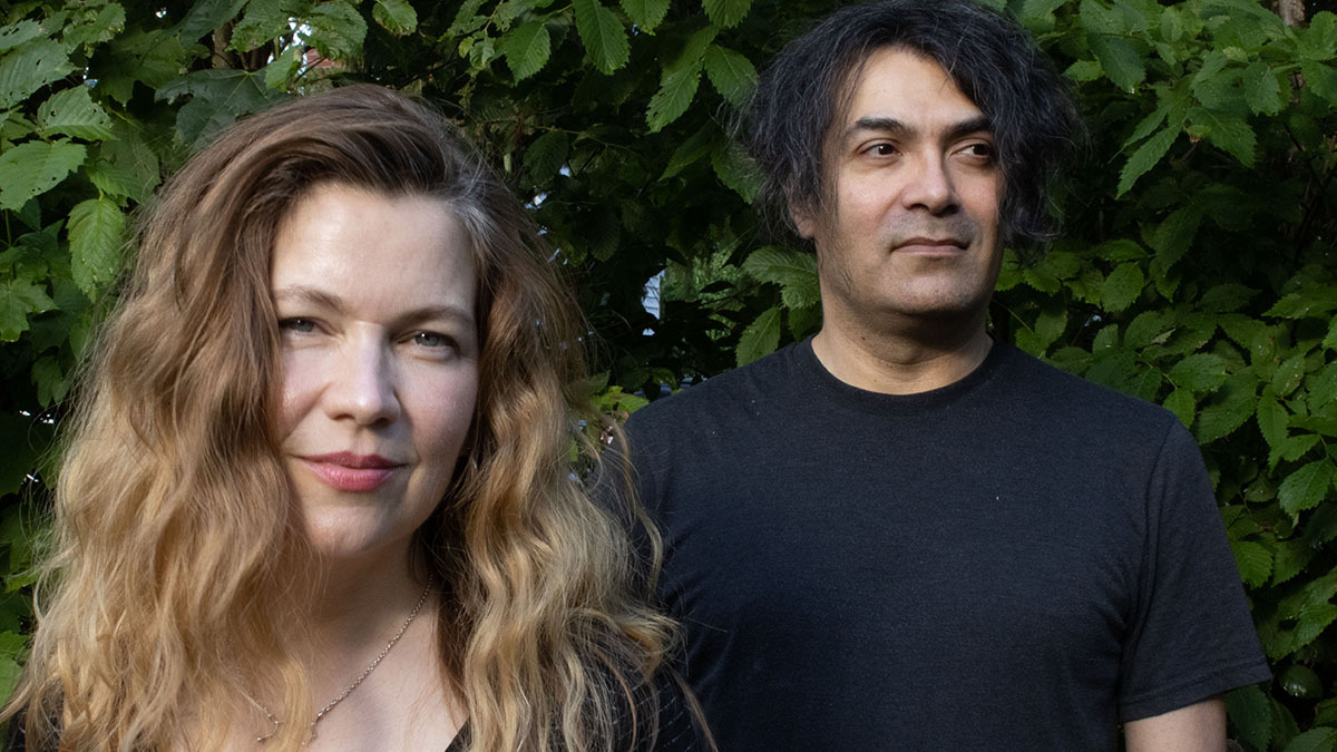 Melissa Arpin Duimstra and Scott Cortez of Lovesliescrushing (who headline Rave Down) stand against a dark background of leafy tree branches; both face the camera, and Arpin Duimstra smiles into the lens while Cortez glances off to one side