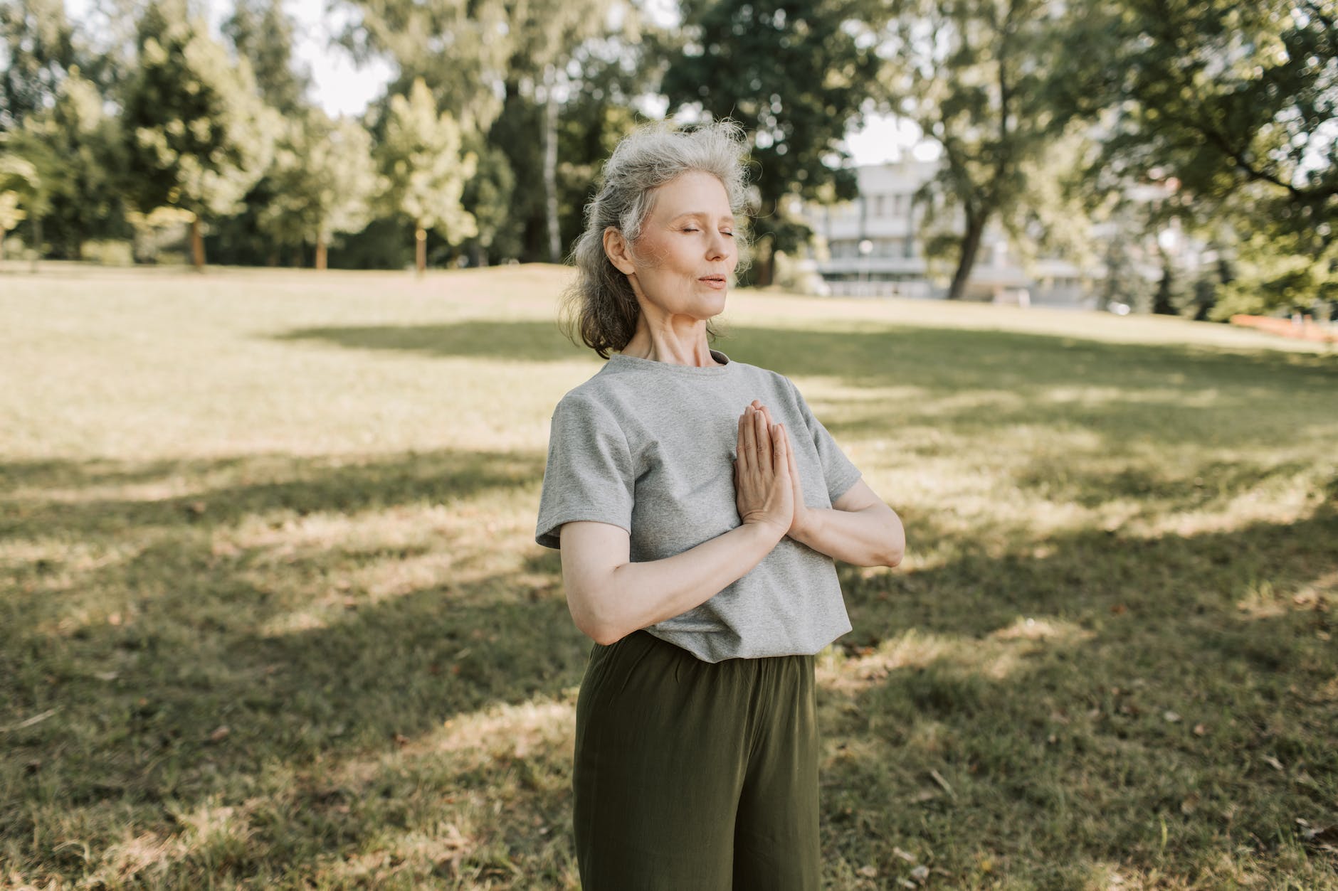 an elderly woman in gray shirt meditating at the park