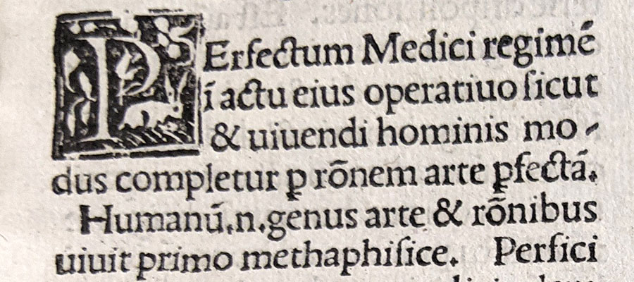 Detail of the first page of a book printed in two columns in Latin with an Illustrated first capital.