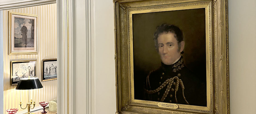 A gold framed painted portrait of a man in military uniform hung on a wall in a hallway.