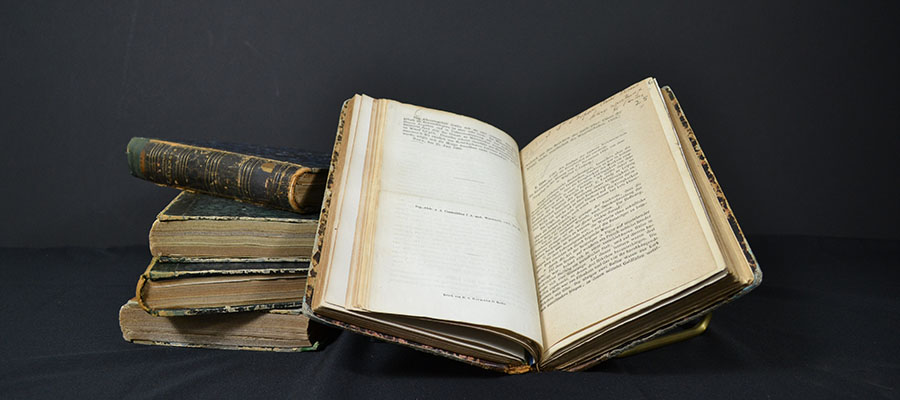 An open volume of books sits atop a pile of closed volumes of books