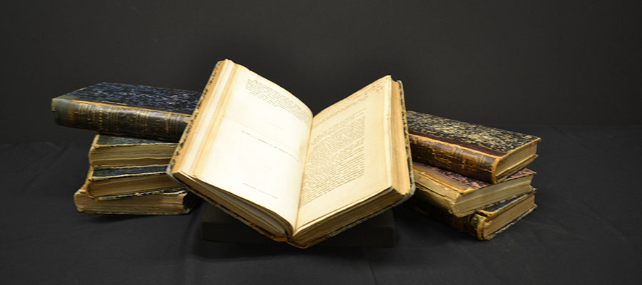 An open volume of books sits atop a pile of closed volumes of books