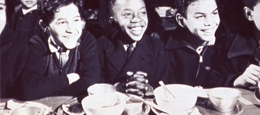 A diverse group of boys grin over finished meals.