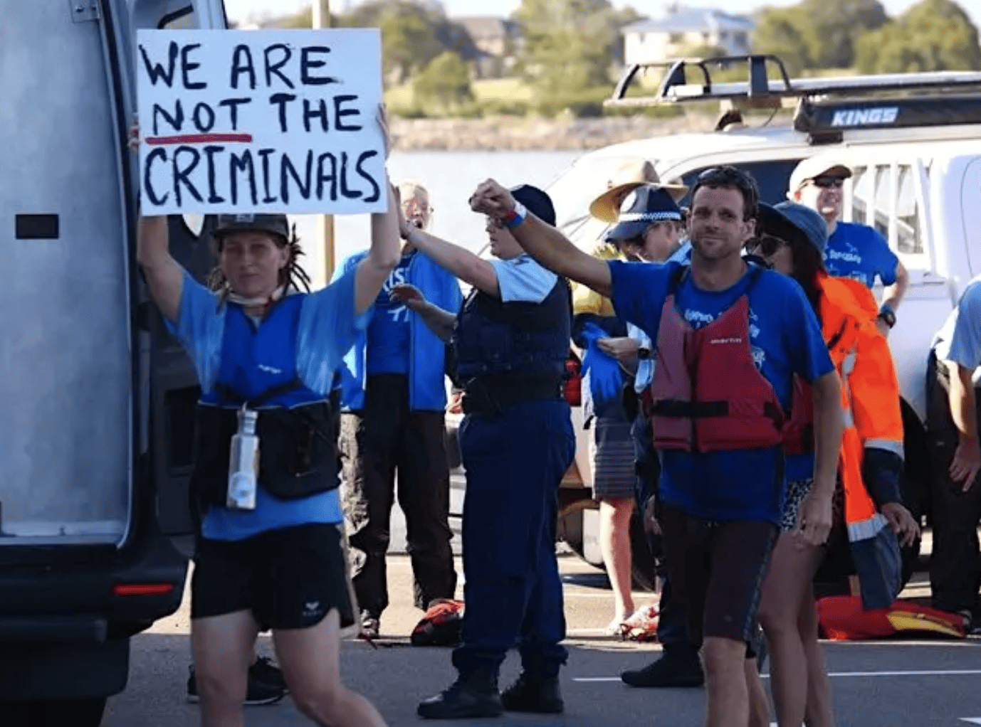 a group of protestors being arrested. One of them is holding a sign that says in capital letters 'WE ARE NOT THE CRIMINALS'. The NOT is underlined in red.