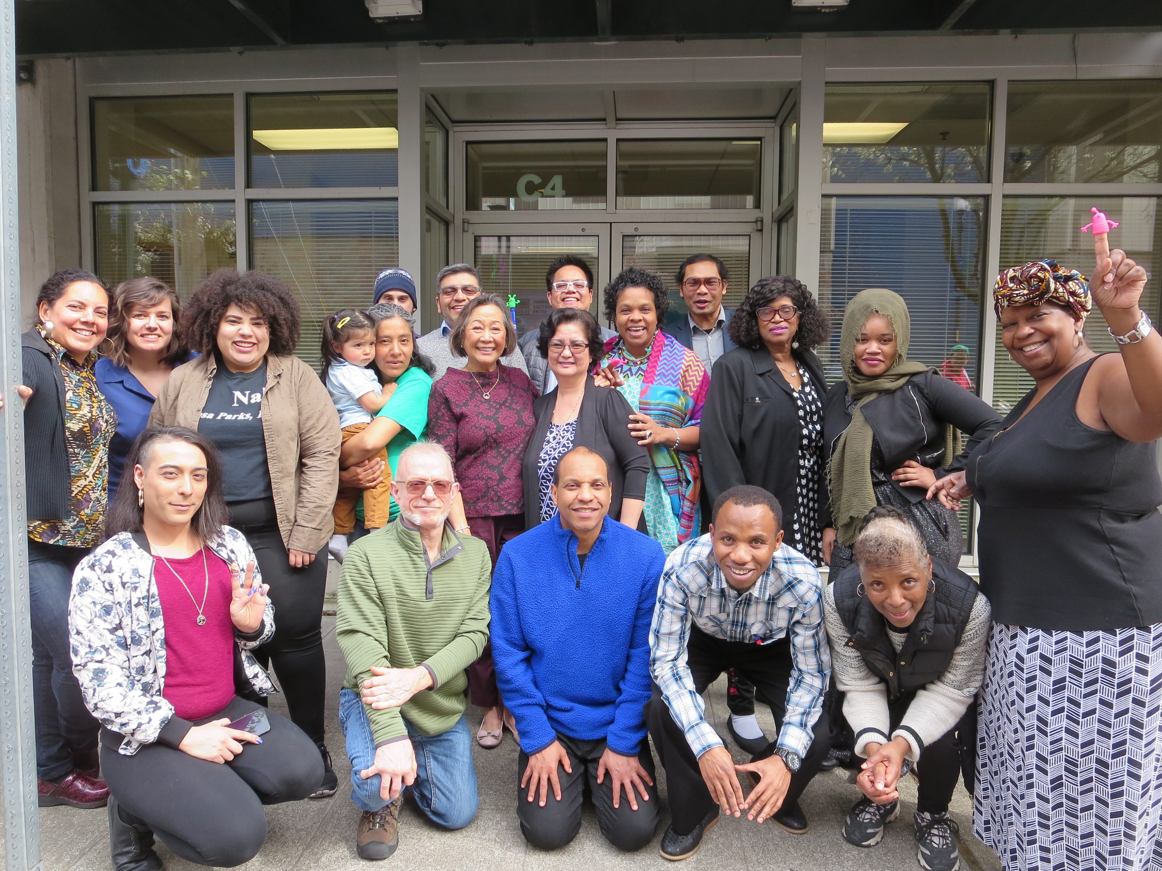 Large posed group photo of 20+ members of Capacity Building Cohort in front of office