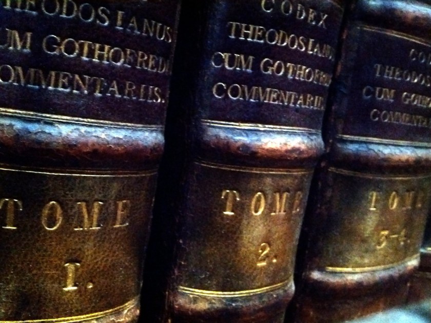 Three antique leather volumes on a shelf. They are three volumes of Codex Theodos Cum, labeled TOME 1, TOME 2, TOME 3-4. Taken at the Royal College of Physicians Library, Regent's Park, London, UK.