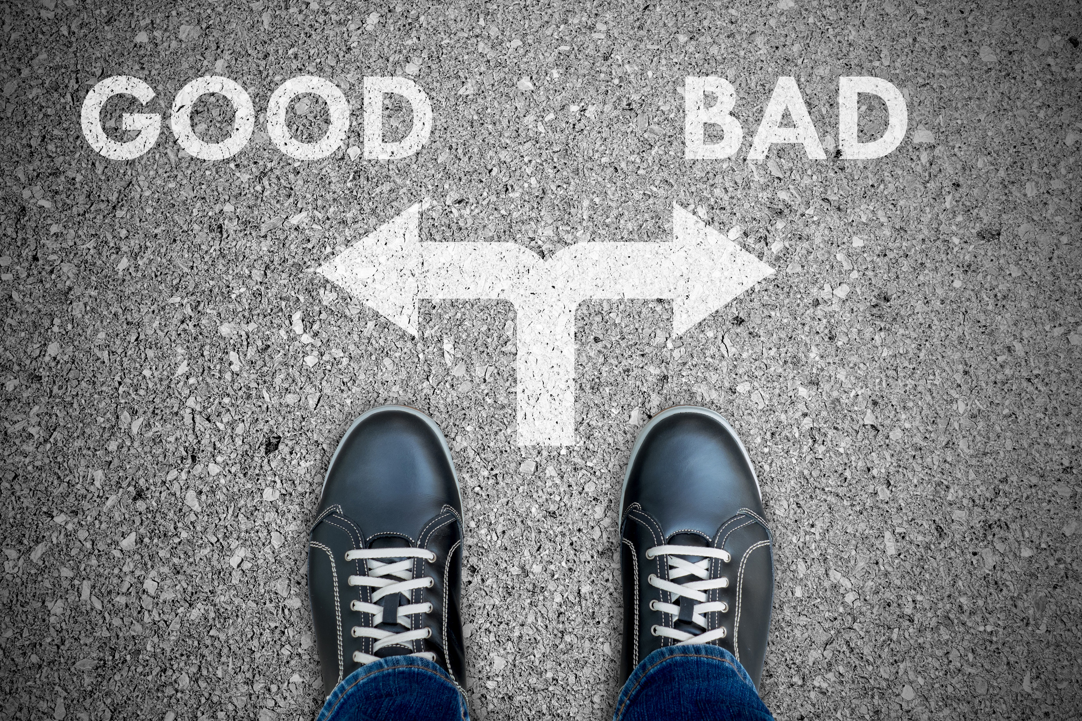 the feet of a person looking at the printed words 'good' and 'bad' on the ground, with an arrow for each word pointing in opposite directions