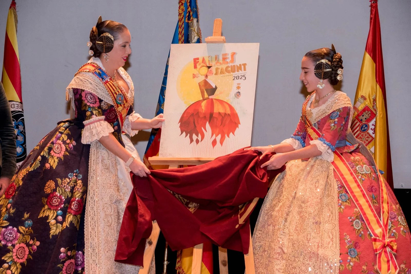 Julia y Teresa mostrando el cartel anunciador de las Fallas 2025