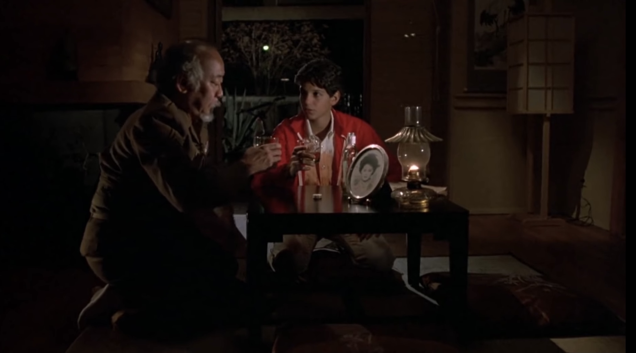 Daniel (Ralph Macchio) sits with a drunken Mr. Miyagi (Pat Morita) in The Karate Kid.
