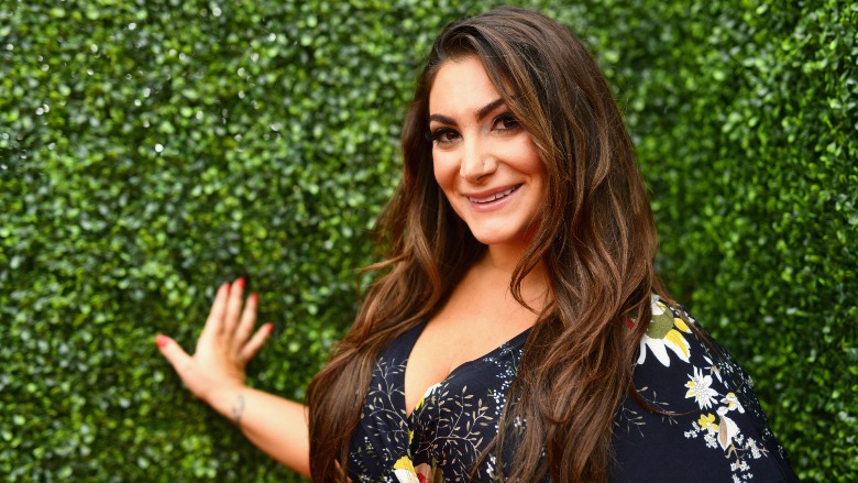 Deena Cortese standing in front of a grass wall.