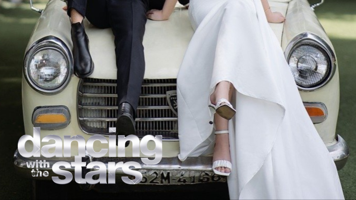 A bride and groom sitting on a car.