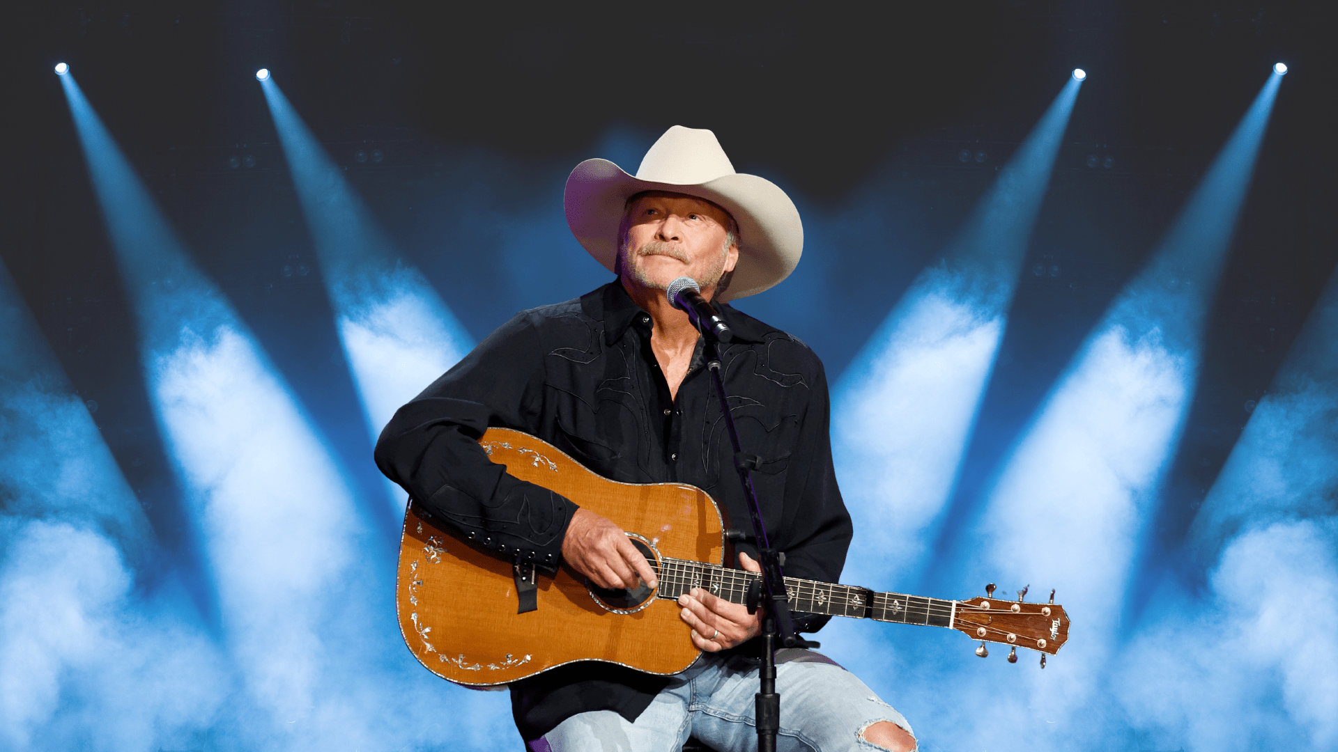 Alan Jackson behind a microphone with a guitar