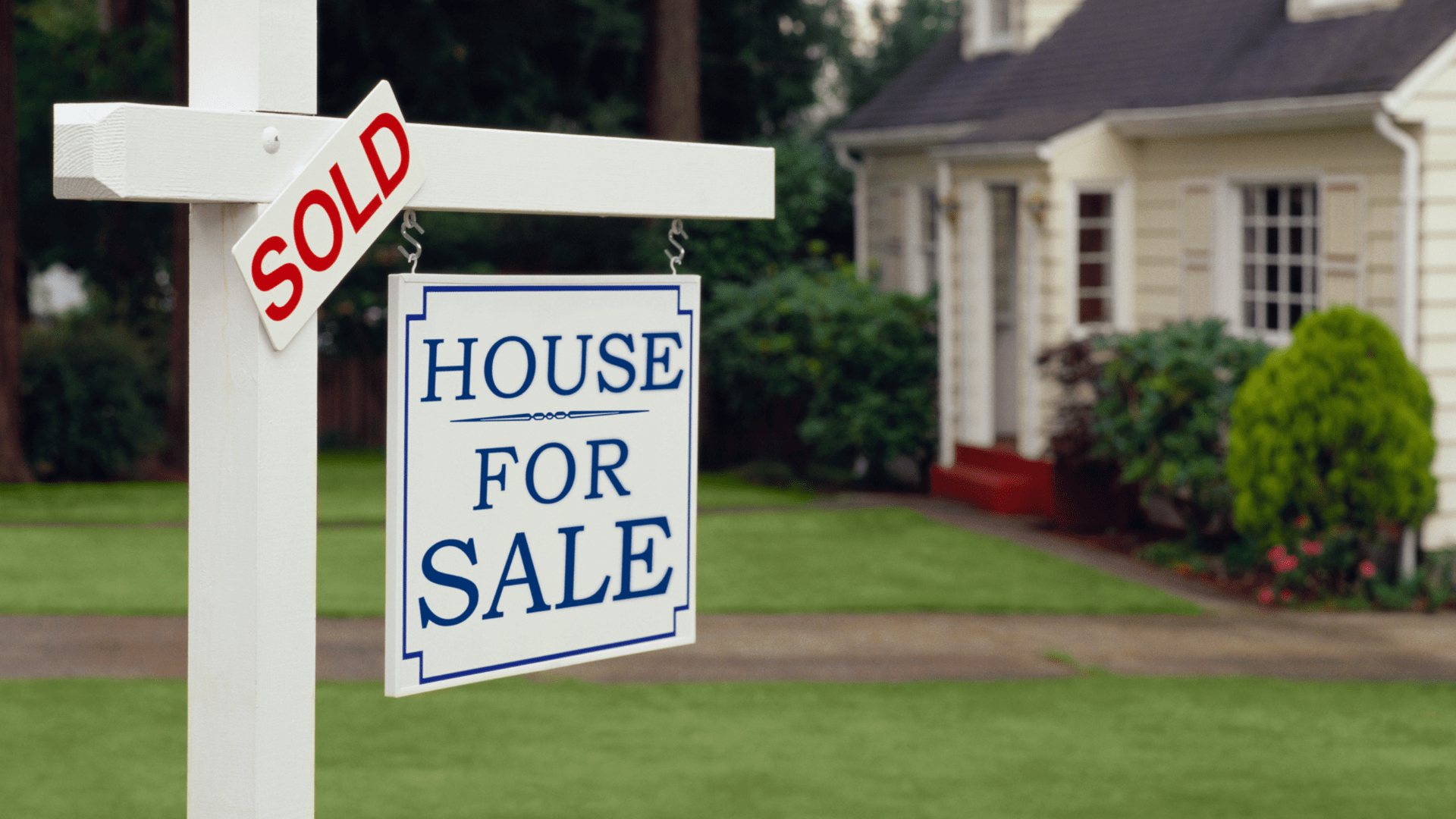 A "sold" sign over top a "house for sale" sign in a yard in front of a house