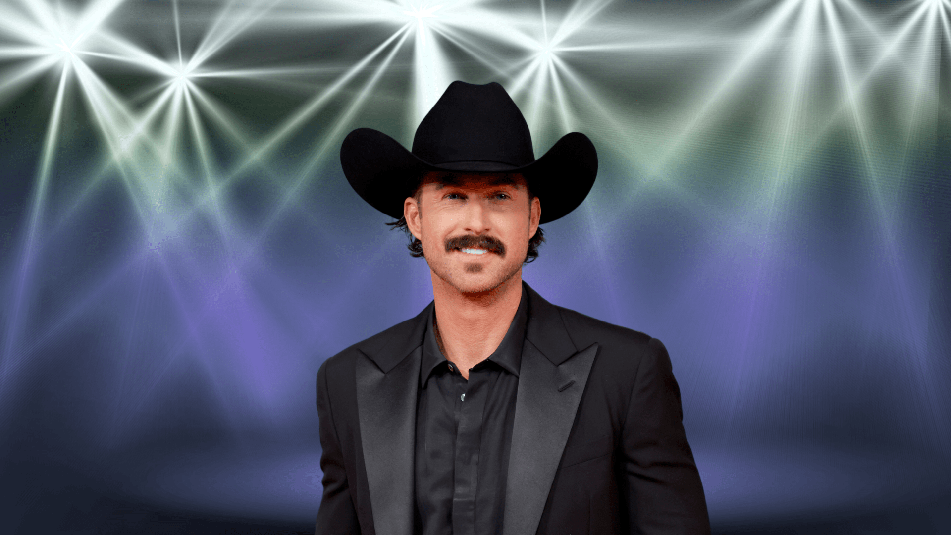 Riley Green posing in an all black formal outfit and cowboy hat.