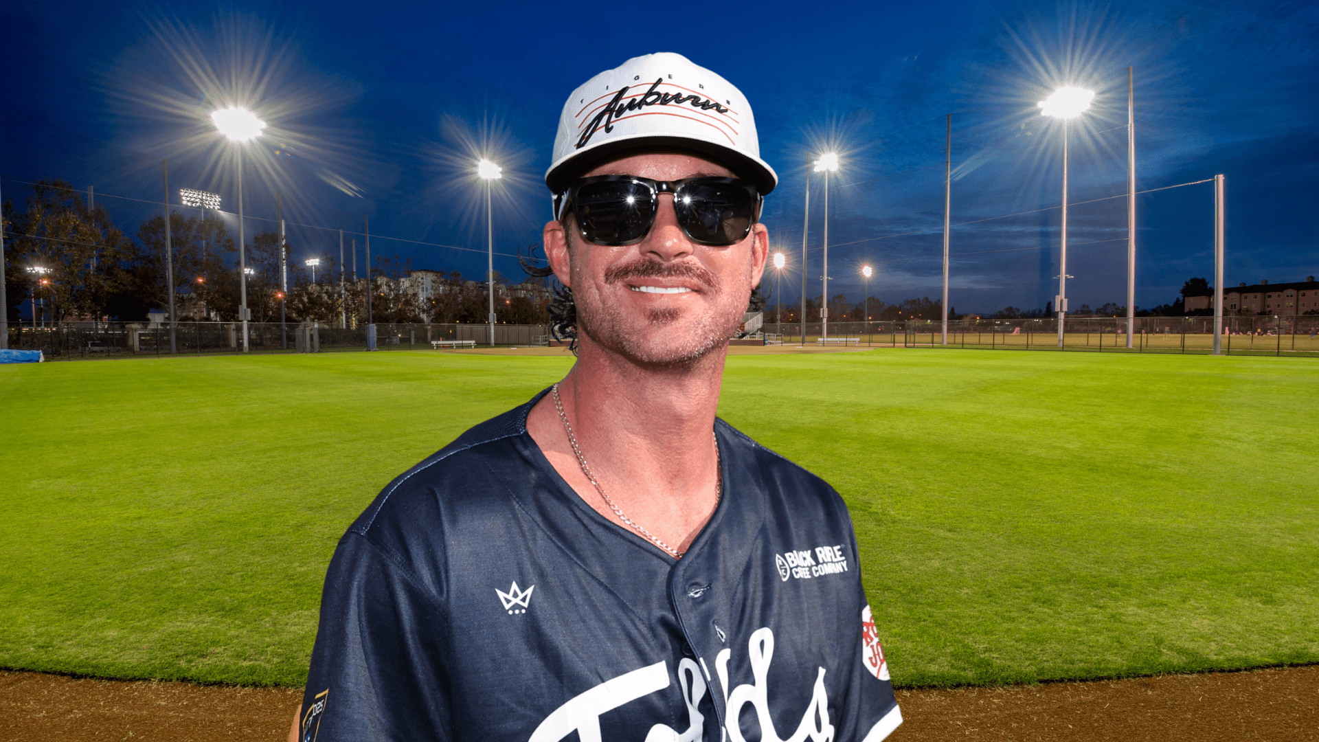 Riley Green posing in sunglasses on a softball field.