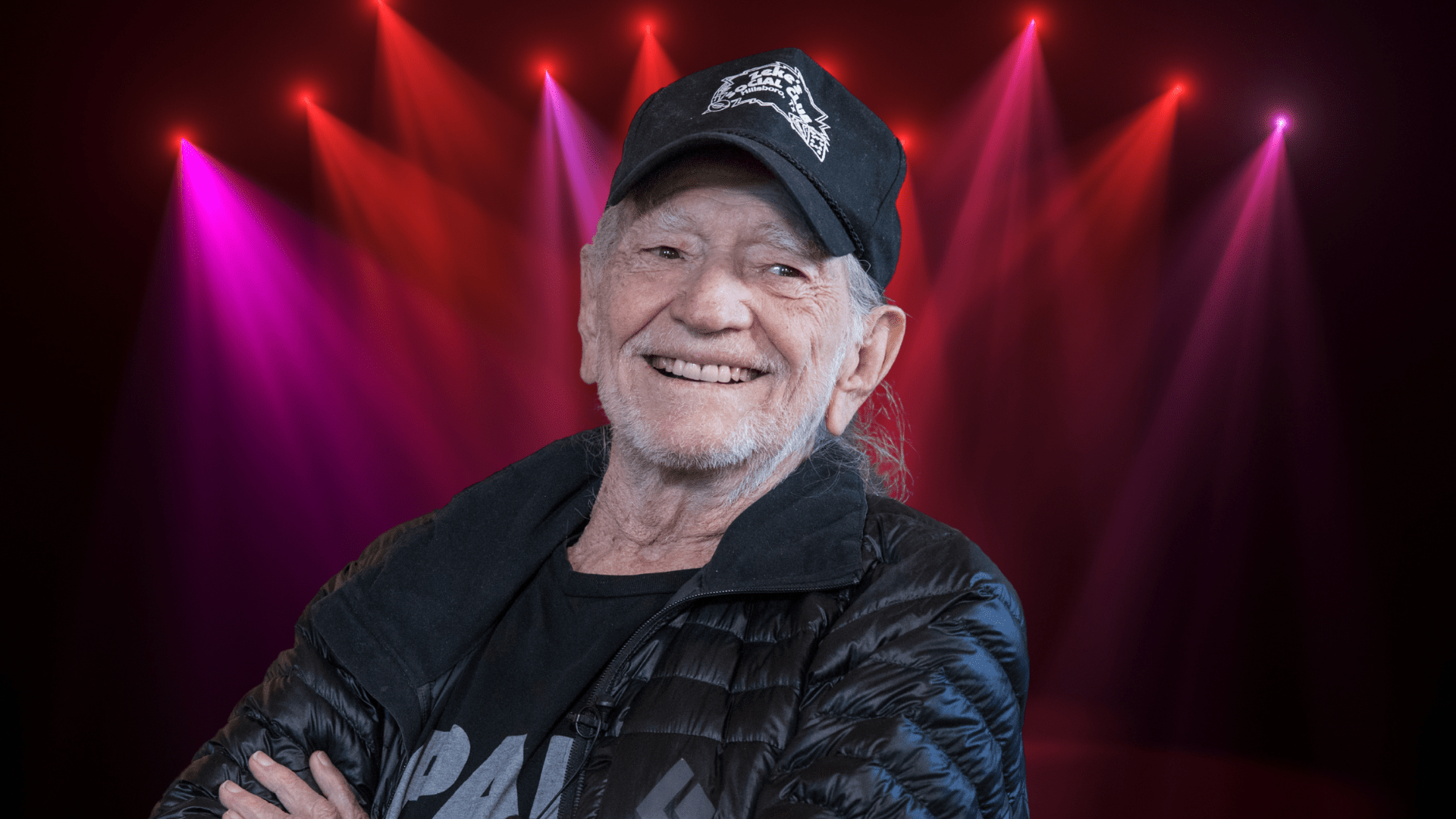 Willie Nelson smiling in front of colorful lights