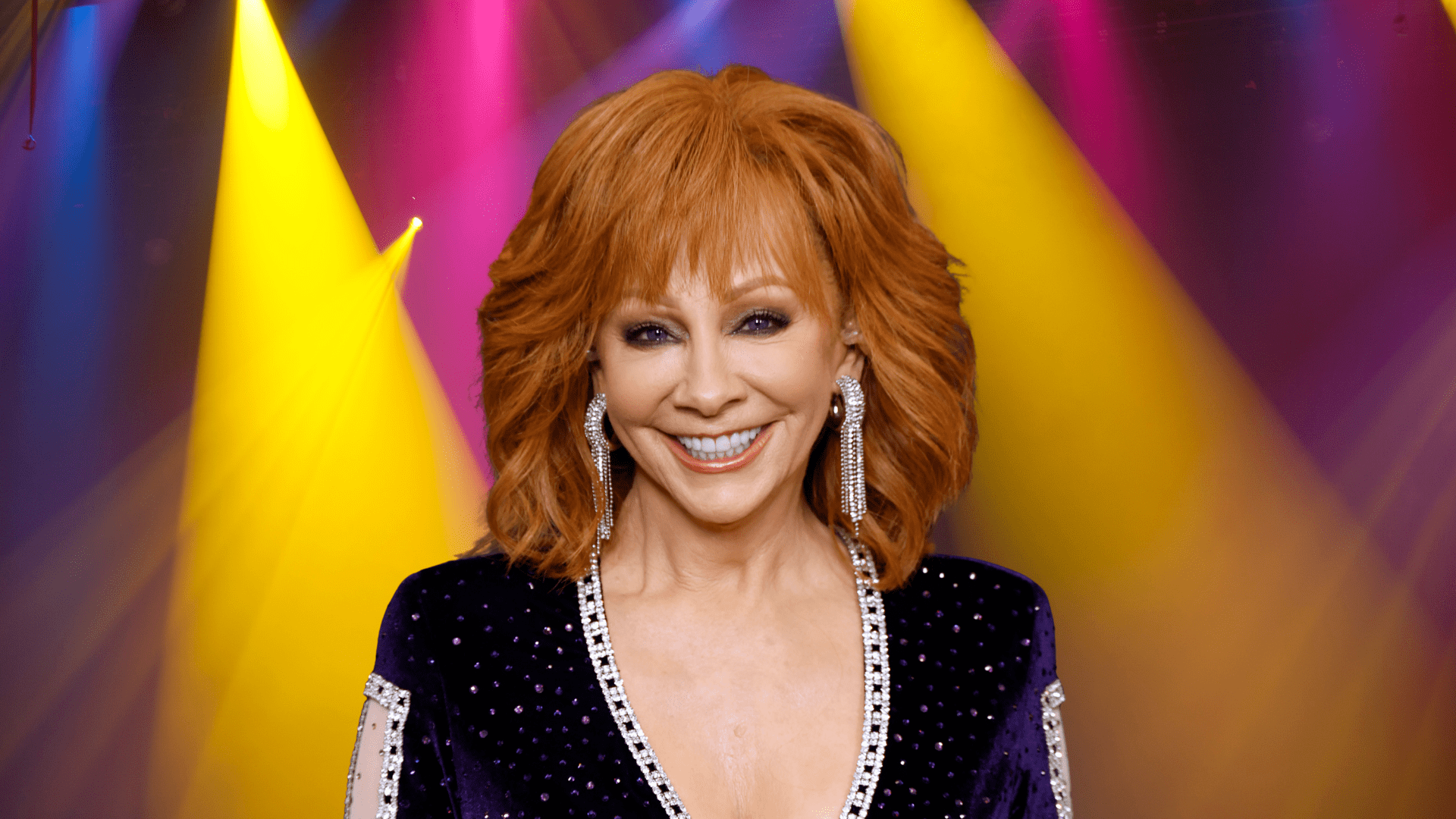 Reba McEntire smiling in front of colorful lights