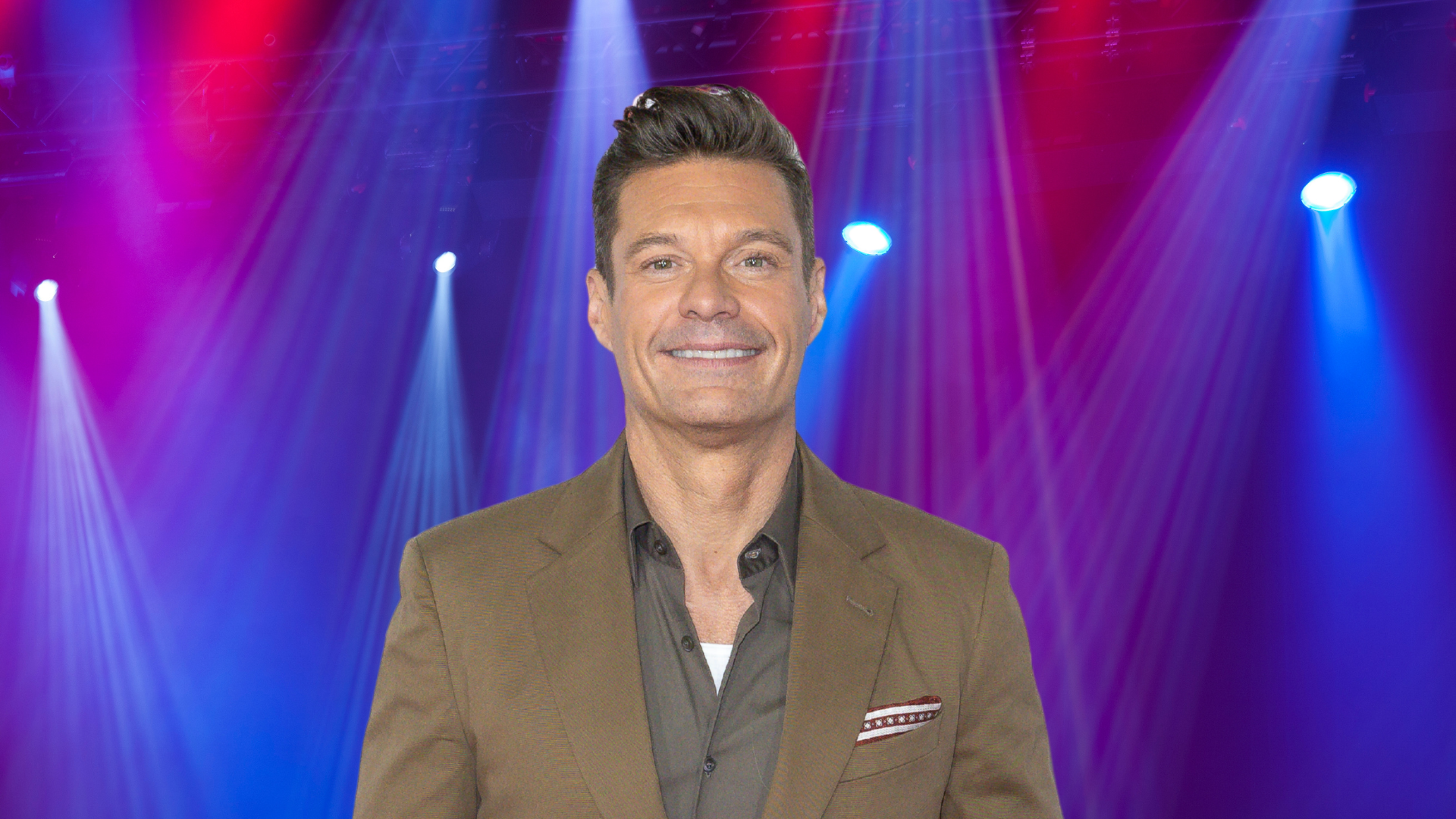 Ryan Seacrest posing on a colorful stage.