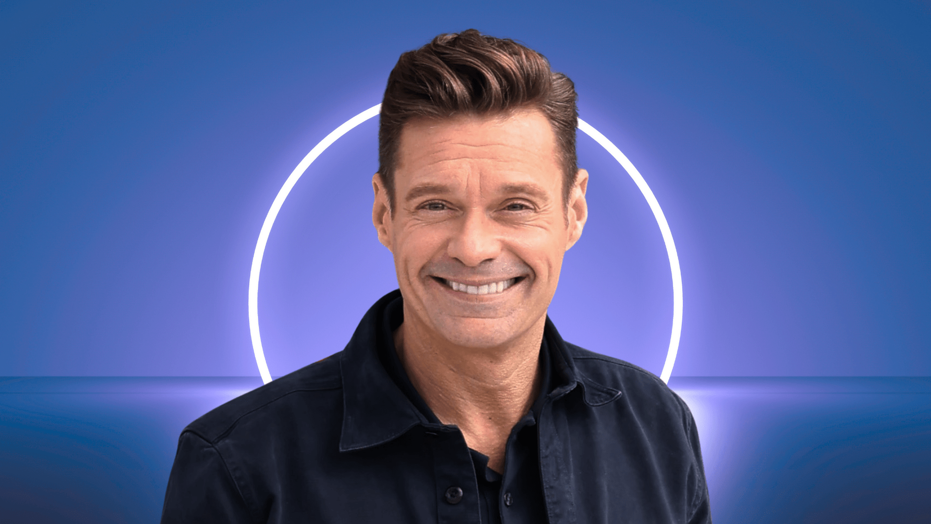 Ryan Seacrest smiling in front of a white light.
