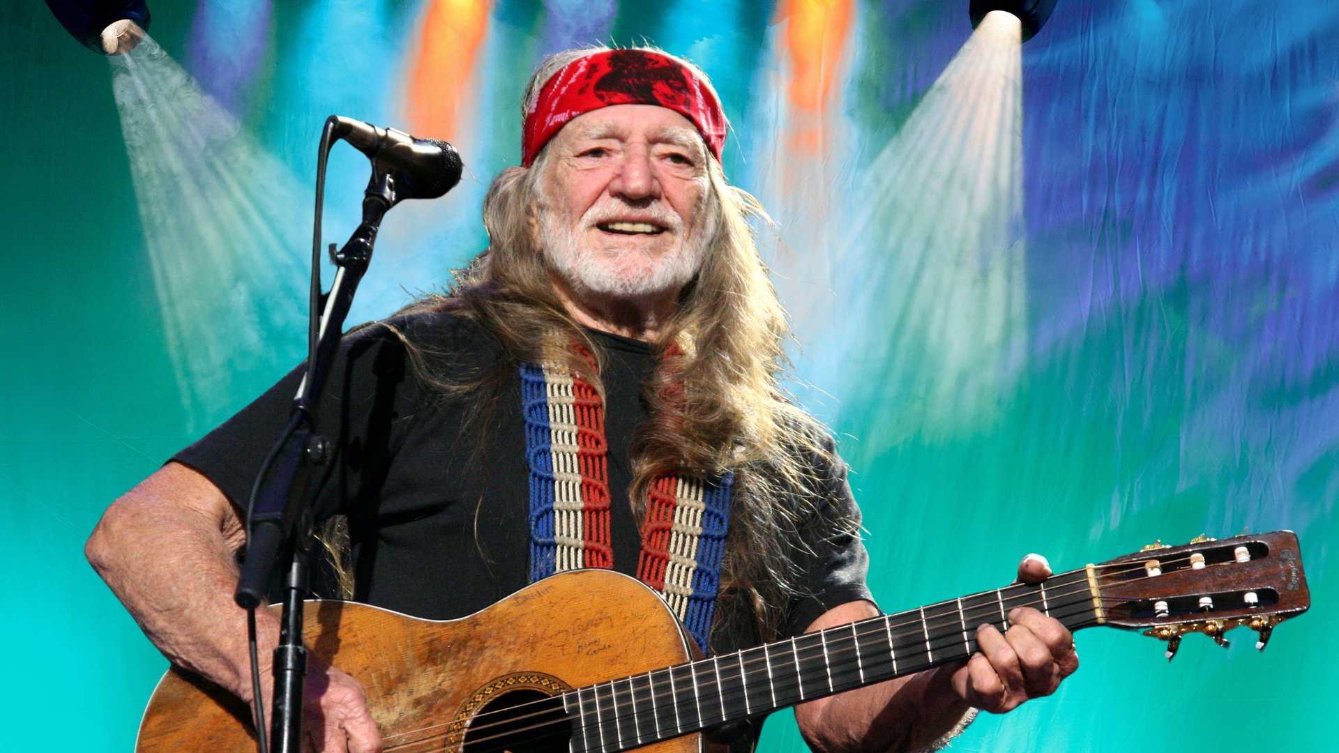 Willie Nelson playing guitar on stage.