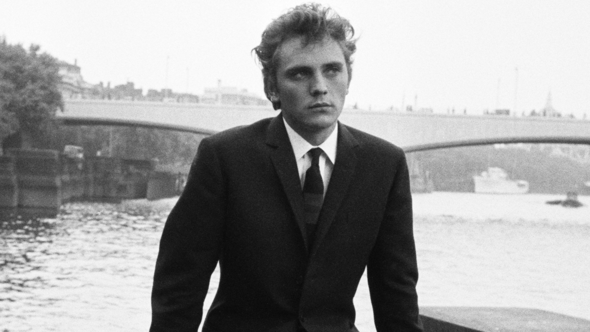 Young Terence Stamp sitting on a bridge