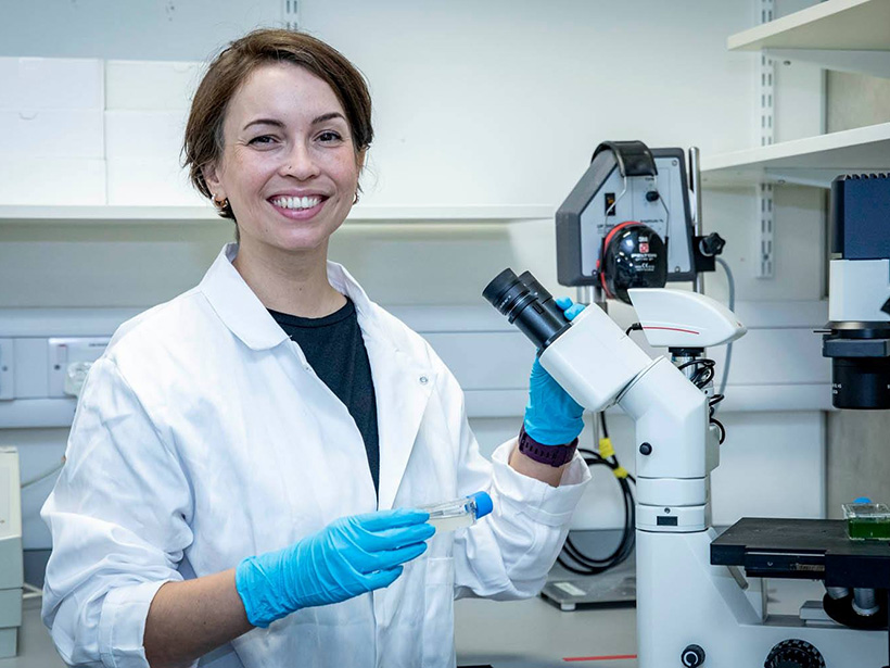 Jacqueline Campbell in a lab with a sample in hand, ready to observe it under a microscope.