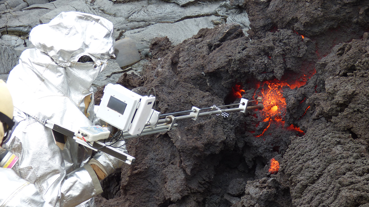 A scientist in a silver suit inserts a long metal tube into glowing orange lava and dark gray rock.
