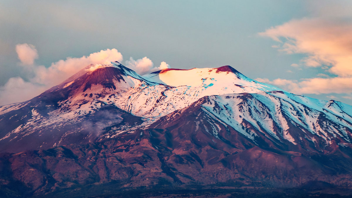 Italy’s Mount Etna, snowcapped and beneath a sky of puffy white clouds.