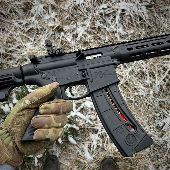 Camouflaged gloved hand holding the M&P 15-22 rifle with a snowy ground for the background