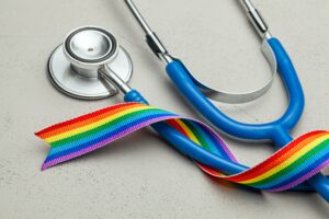 A blue stethoscope on a table with a rainbow ribbon