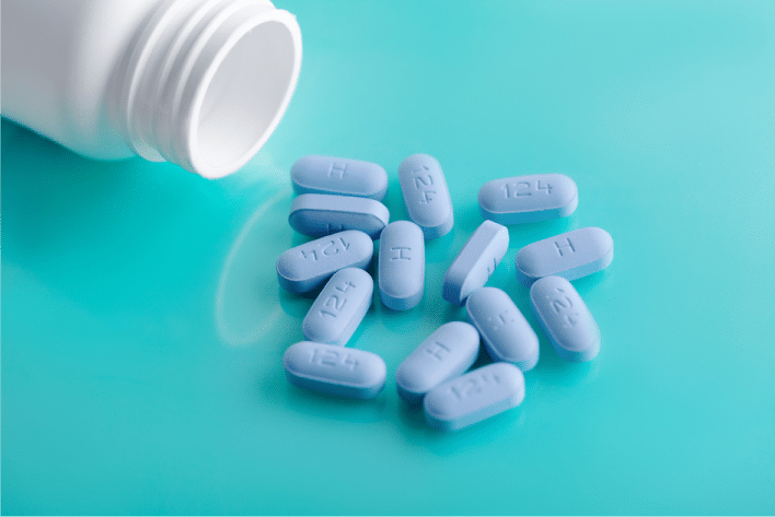 photo of white prescription bottle and several blue pills on an aqua background