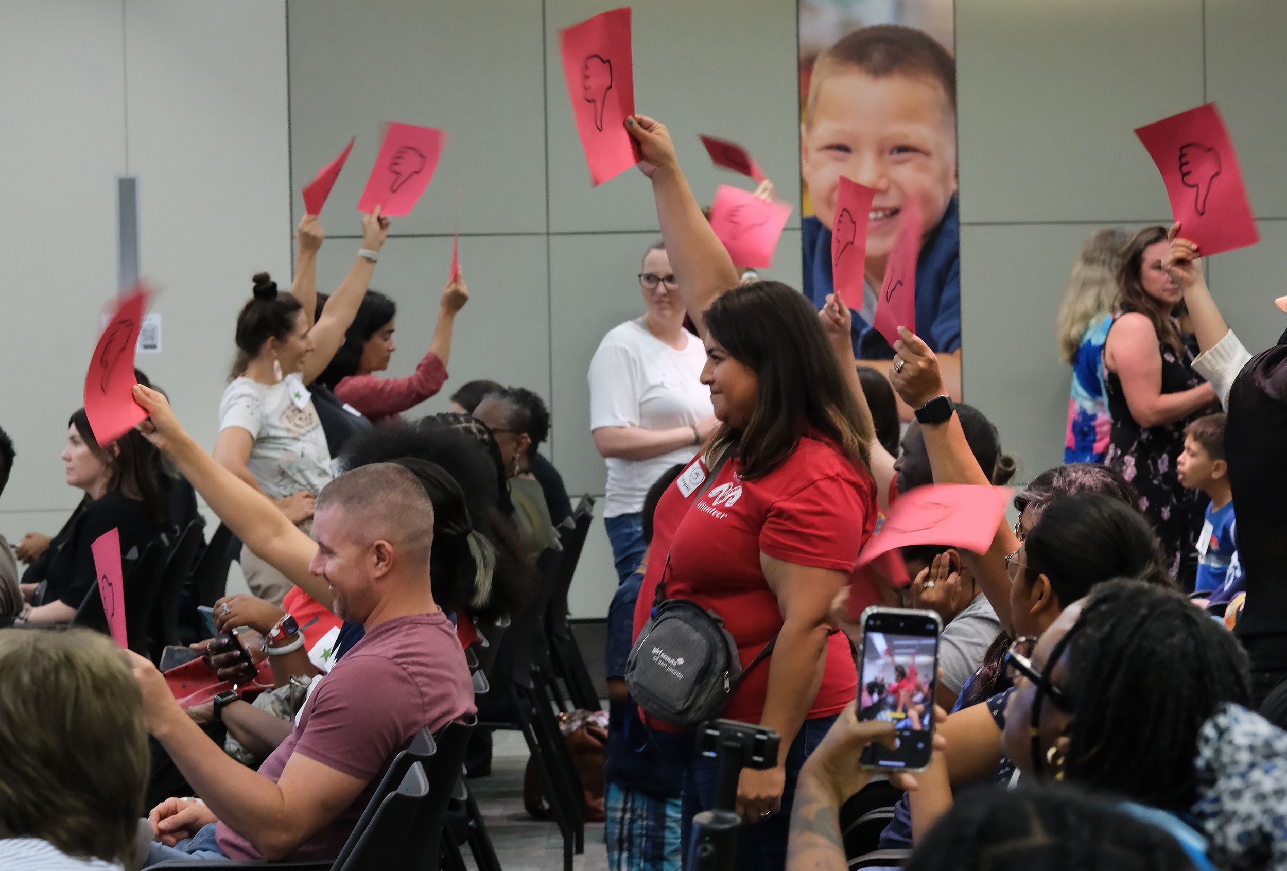 Community members attending Houston ISD's school board meeting stand and hold ‘thumbs down” signage in opposition to Superintendent Mike Miles' plans