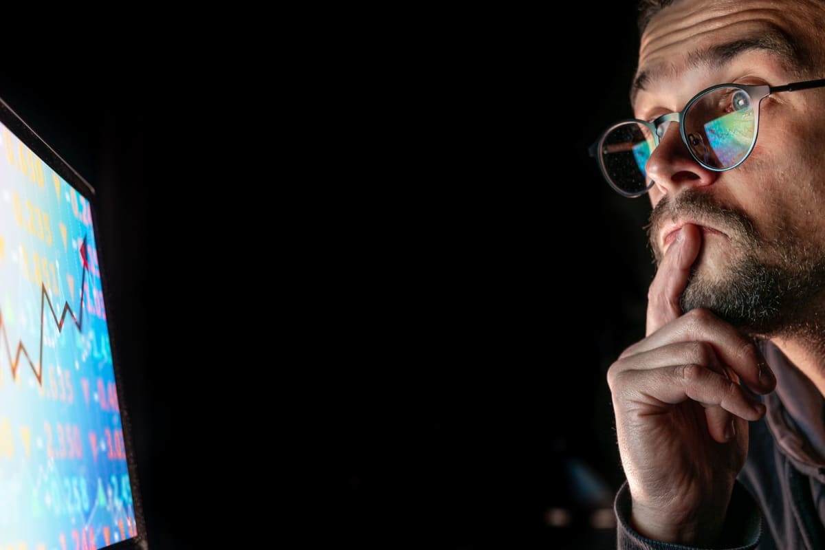 Homem analisando gráficos: Google Tag Manager homem de barba e óculos de grau com a mão no queixo olhando de forma concentrada para o monitor a sua frente