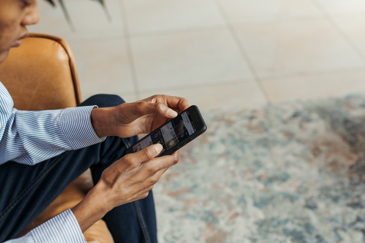 homem sentado mexendo no celular homem negro, com blusa social listrada, sentado mexendo no celular
