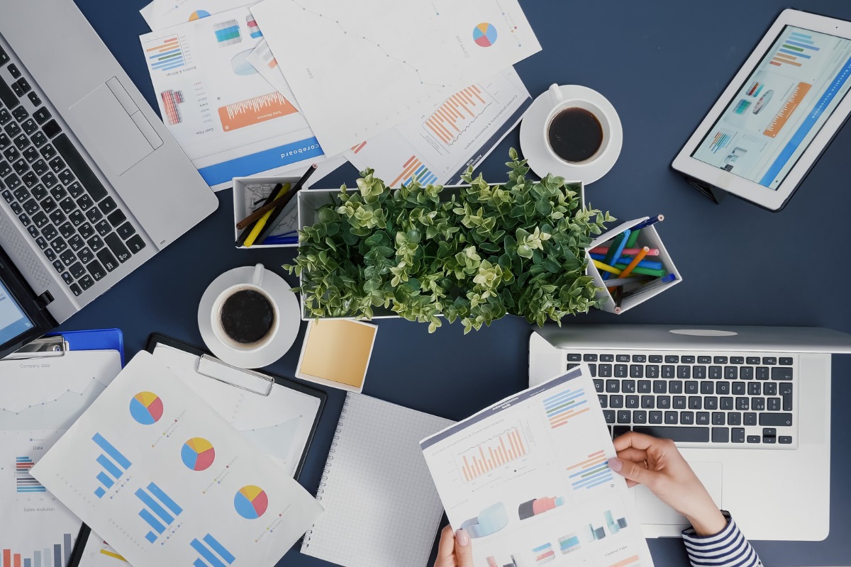 mesa com vários relatórios: público-alvo mulher sentada em uma mesa com vários relatórios com gráficos espalhados.