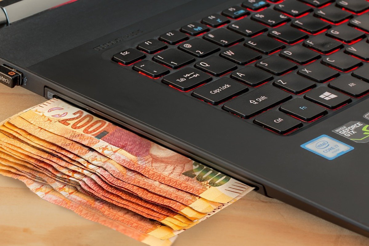 laptop com dinheiro saindo dele: público-alvo laptop com a parte onde fica o espaço para CD apresentando notas de 200 saindo, como se fosse o caixa de um banco