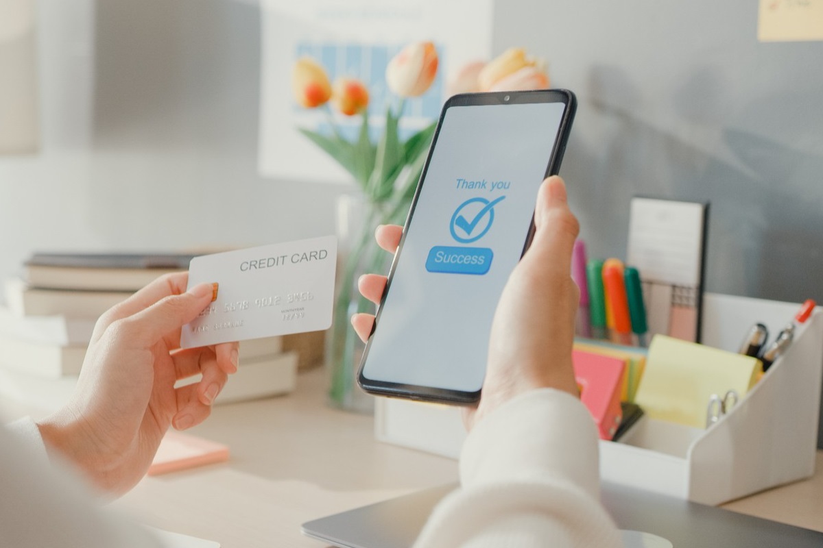 pessoa fazendo uma compra online: remarketing pessoa segurando um celular com uma mão e um cartão de crédito com outra, dando a entender que está fazendo uma compra online