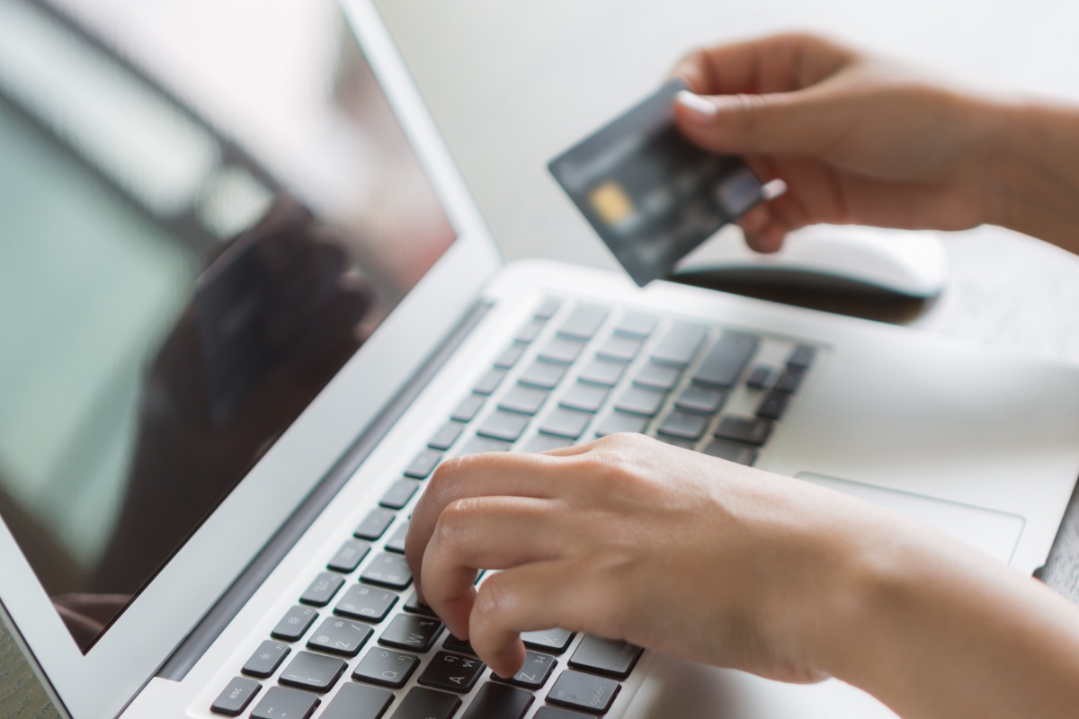 pessoa fazendo uma compra virtual: remarketing pessoa usando o laptop enquanto segura um cartão de crédito, parecendo estar fazendo alguma compra online