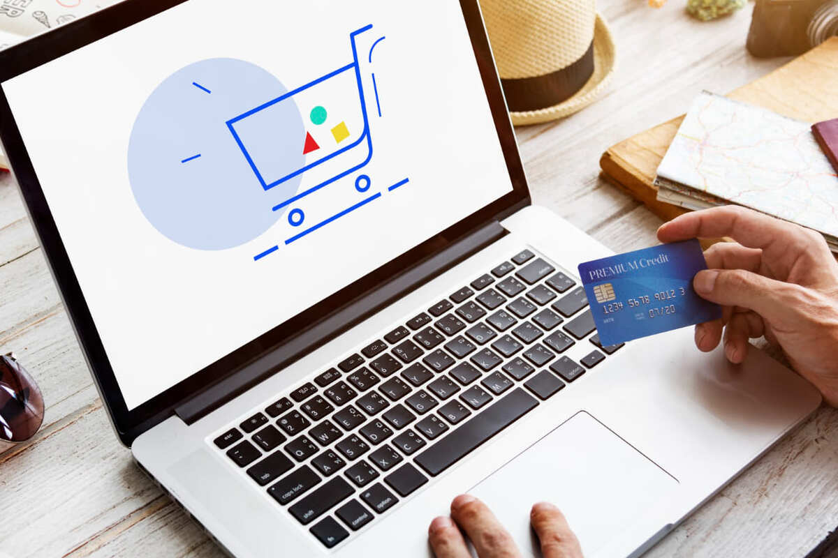 homem com cartão de crédito: remarketing homem usando um laptop e segurando um cartão de crédito. Na tela do computador há um ícone de carrinho de compras