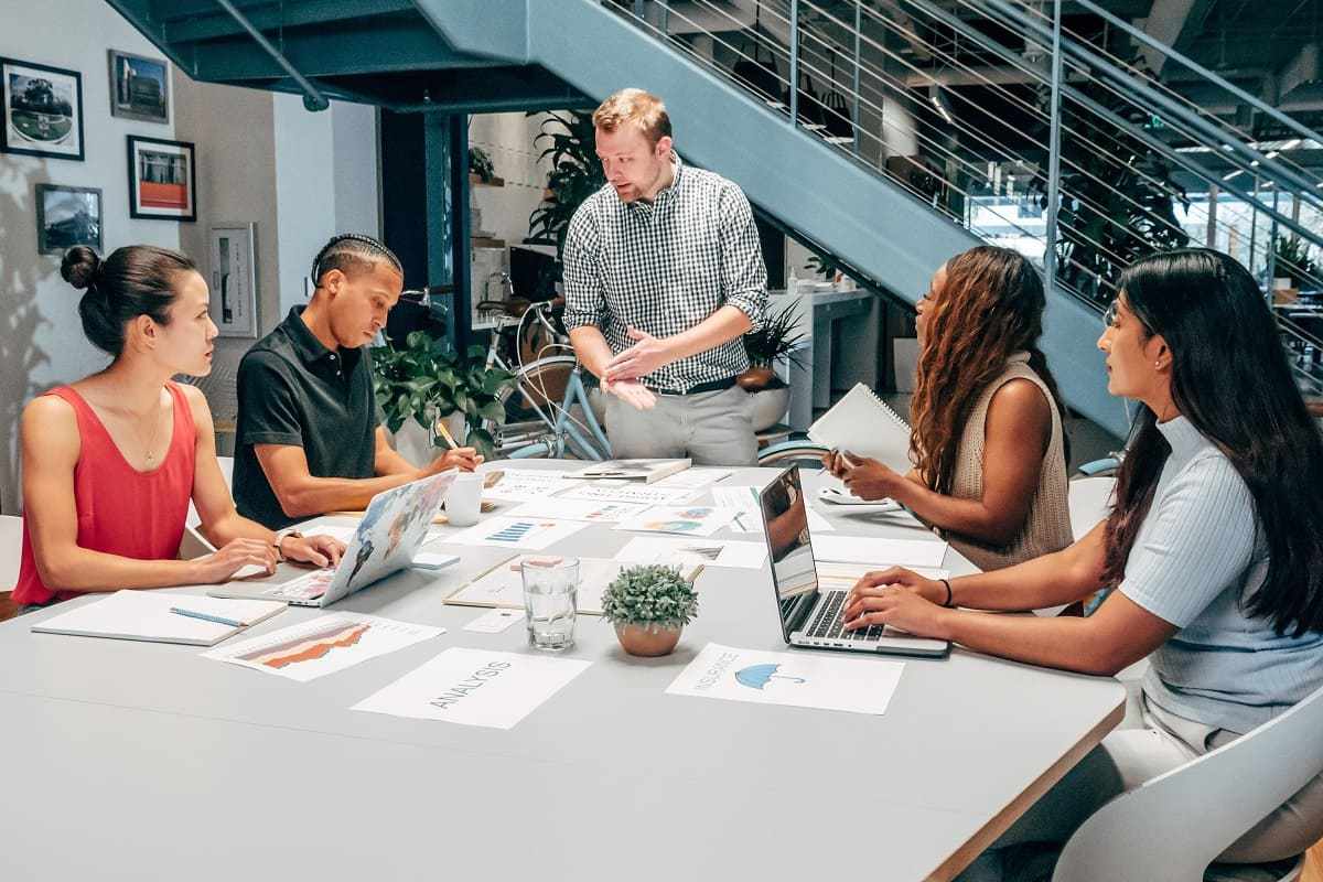 pessoas em reunião: plano de marketing pessoas sentadas em uma mesa de reunião, enquanto um homem está de pé